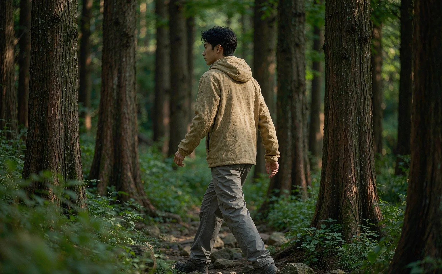 Side view of a person walking through a forest trail in a GRS recycled fleece mid-layer