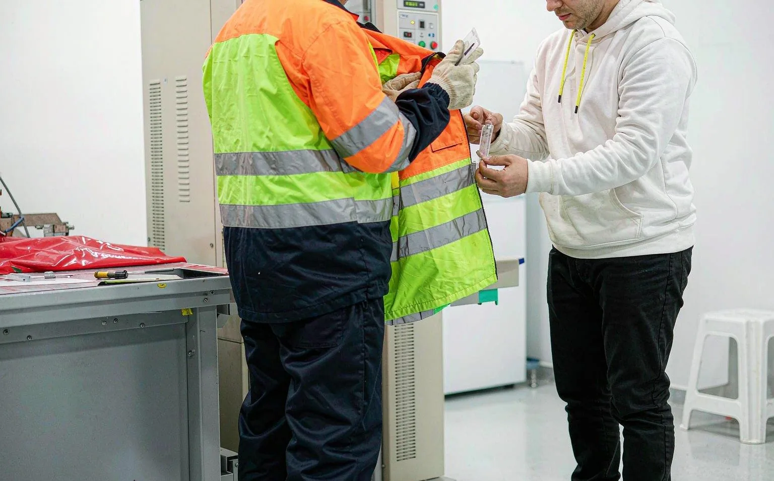 Side and back view of inspectors checking EN ISO 20471 hi-vis workwear compliance in a testing lab
